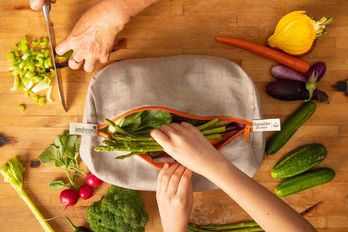 Hands zipping fresh produce into a linen Ambrosia bag