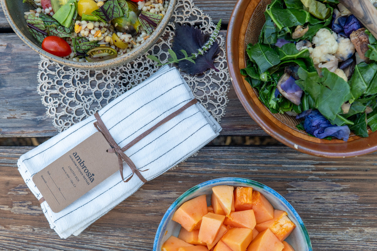 Linen napkin set on a table with bowls of grain salad, greens, and papaya