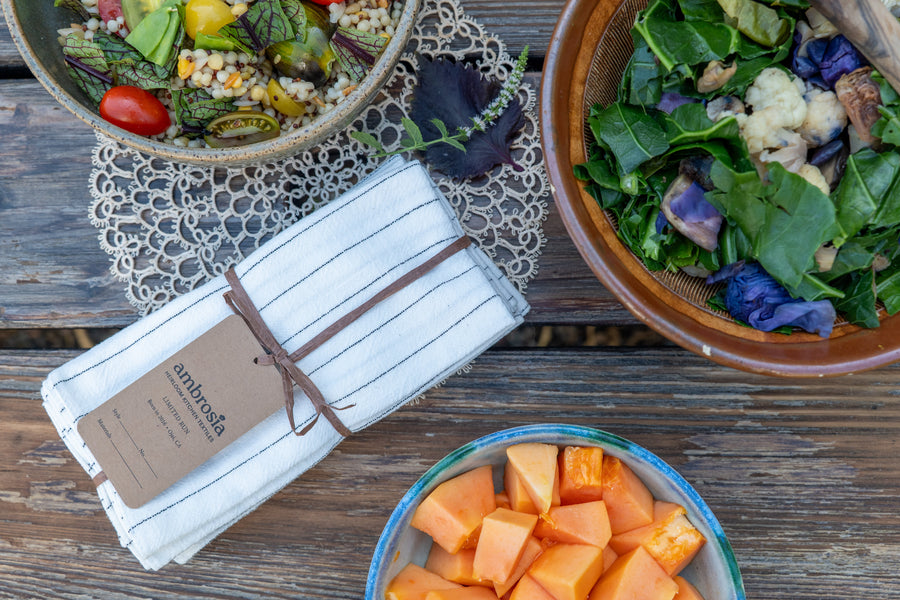 Linen napkin set on a table with bowls of grain salad, greens, and papaya